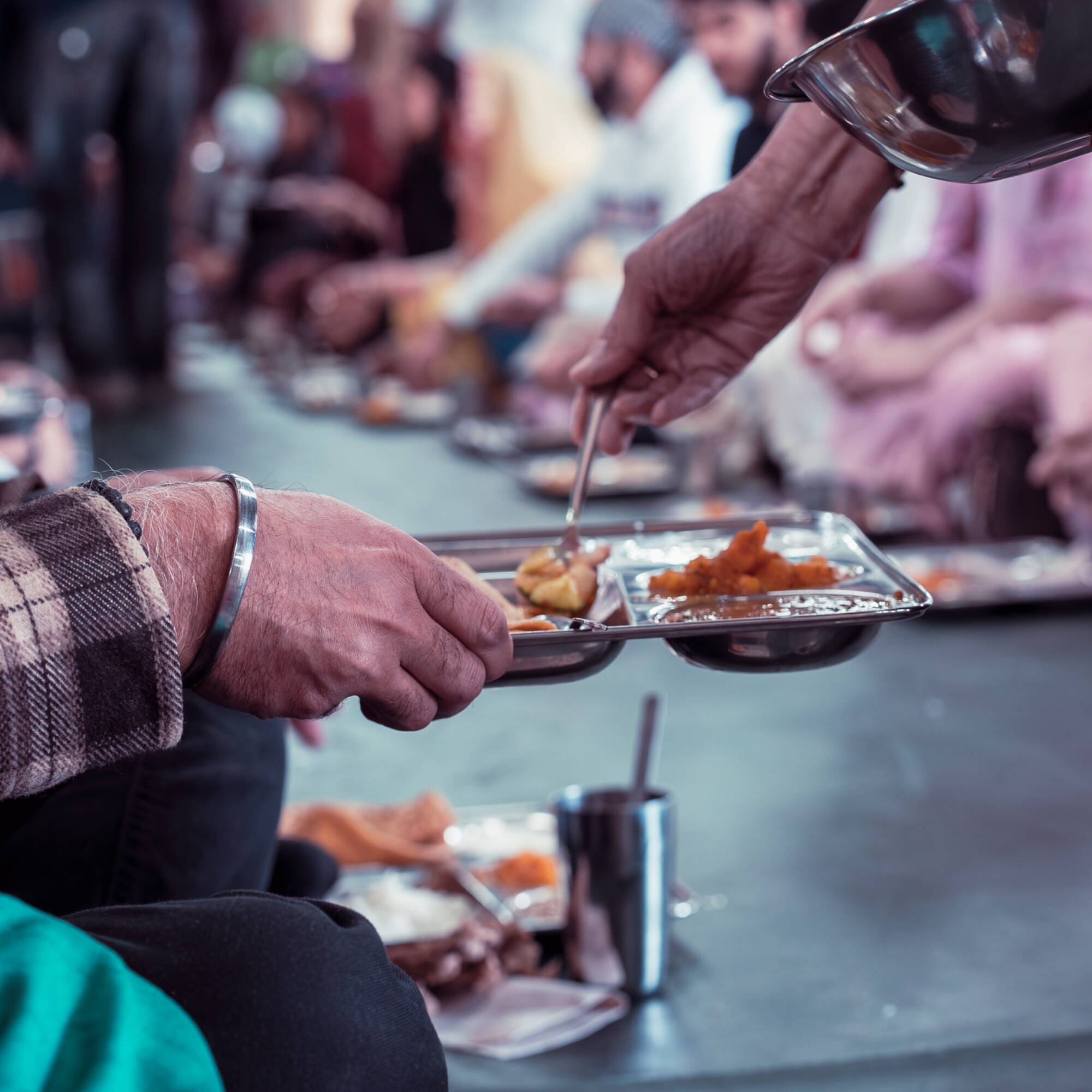 A close-up of of a tray being filled with food held by a man with a silver bracelet, or kara.